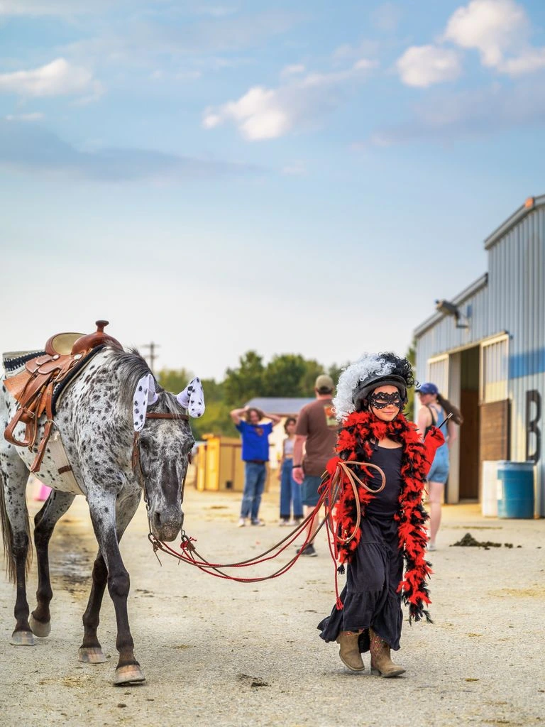 A spotted pony stands with lowered head in a round pen while her handler waits relaxed at the center.